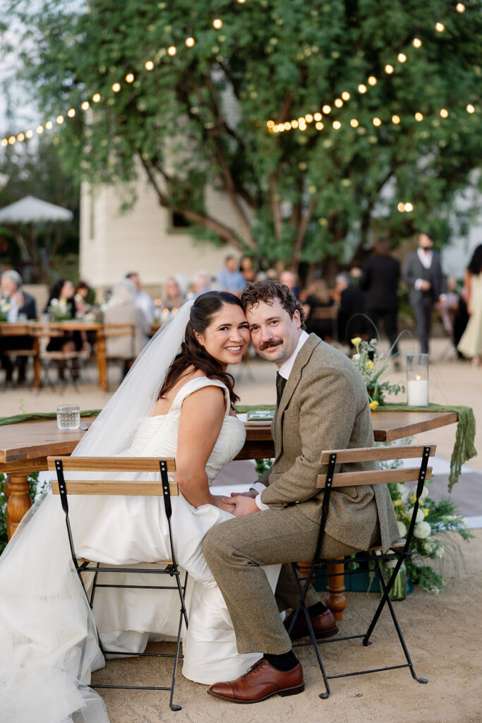 Bride and groom smiling while seated at their sweetheart table at The Swanner House in San Juan Capistrano, CA.