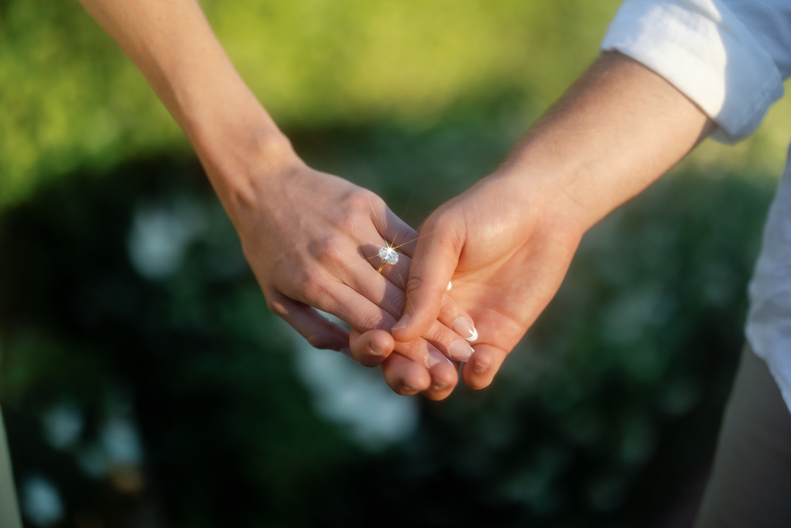 Wide shot of a couple holding hands with an engagement ring shining from the light.