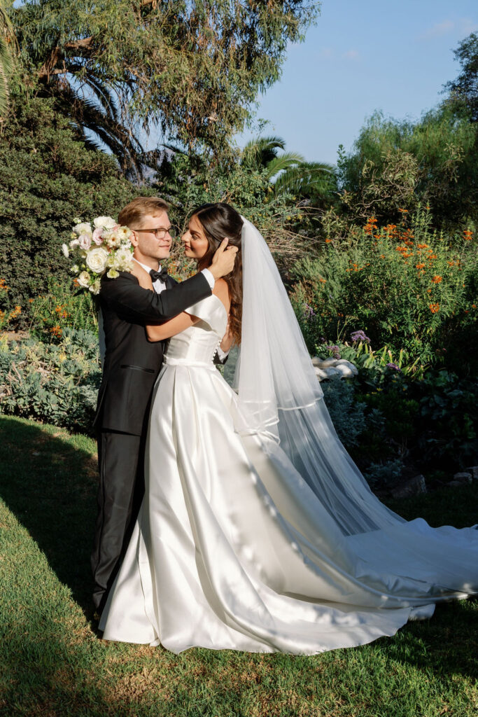 Groom holding the bride close in the garden with warm sunset light behind them at McCormick Home Ranch.