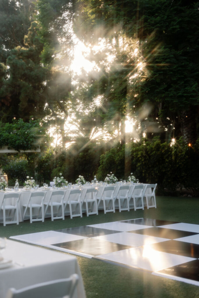 Long reception tables set on the circular lawn at McCormick Home Ranch during golden hour, with sunlight streaming through the trees.