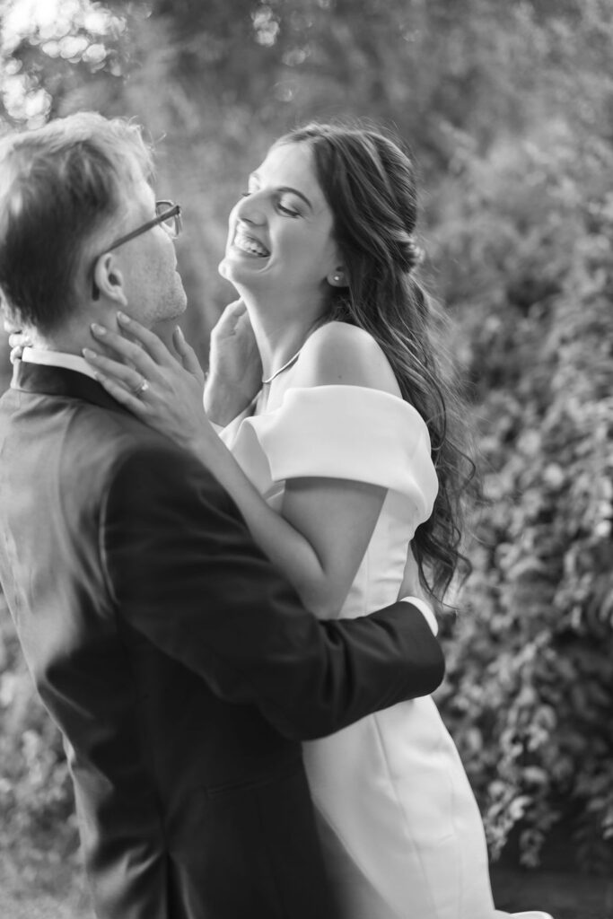 Black and white candid of the bride laughing while holding her partner during portraits.