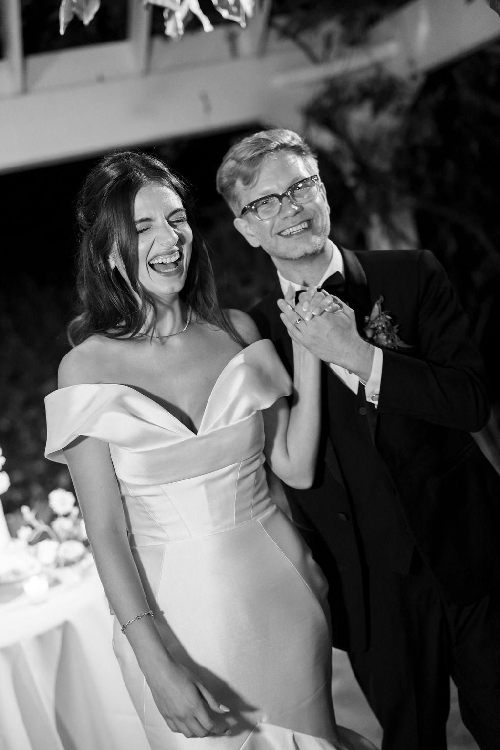 Black and white candid of the couple laughing and holding hands during their reception.
