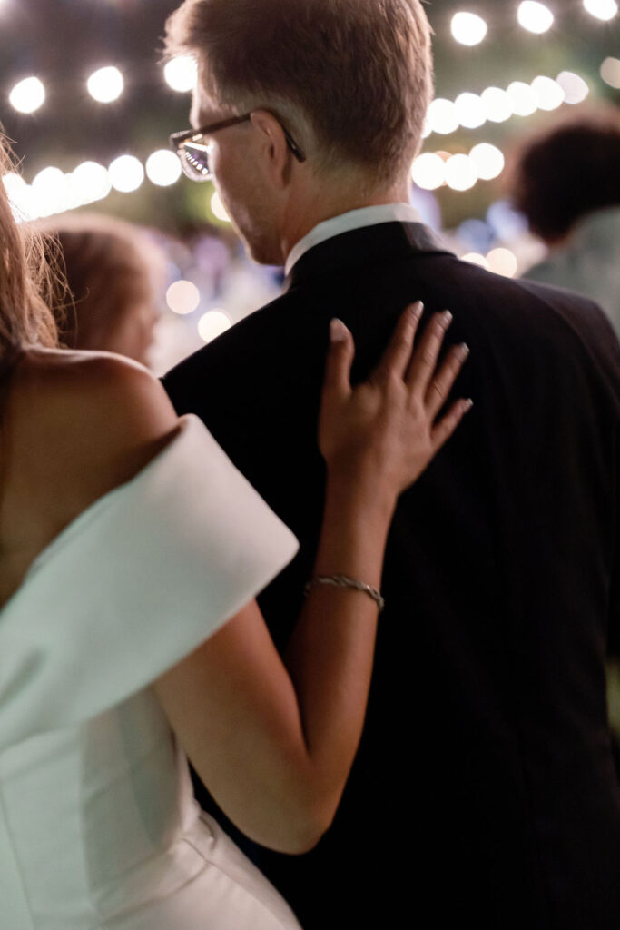 Close-up of the bride resting her hand on her partner’s back during the nighttime reception at McCormick Home Ranch.