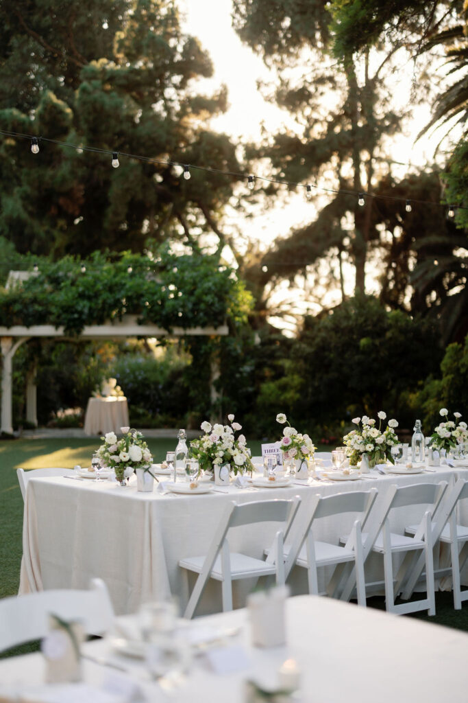 Long reception tables set on the circular lawn at McCormick Home Ranch during golden hour, with sunlight streaming through the trees.