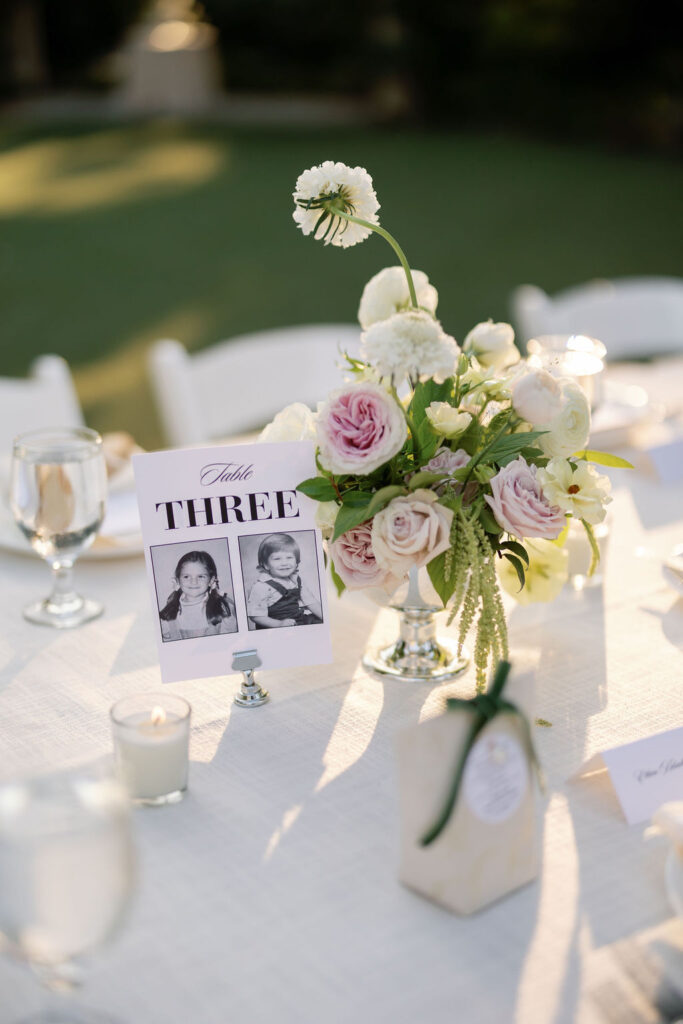 Floral centerpiece and table number with childhood photos at the McCormick Home Ranch circular lawn reception.