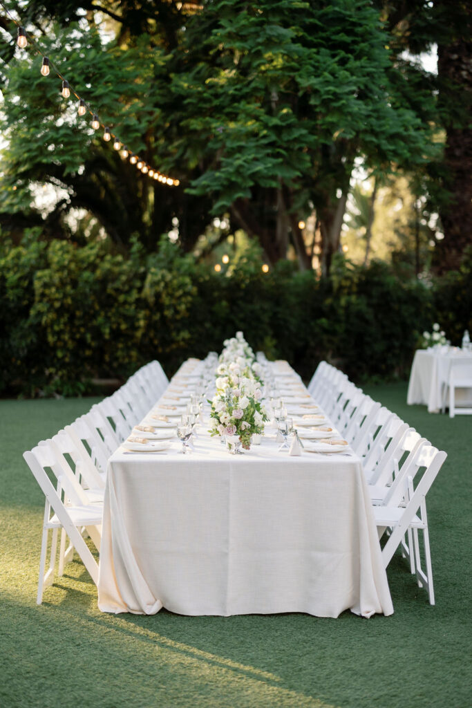 Long reception tables set on the circular lawn at McCormick Home Ranch during golden hour, with sunlight streaming through the trees.