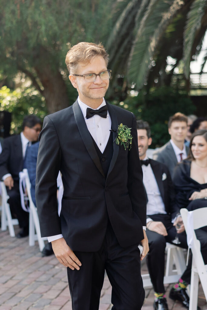 Groom smiling as he walks down the aisle in a black tuxedo during the outdoor ceremony at McCormick Home Ranch.