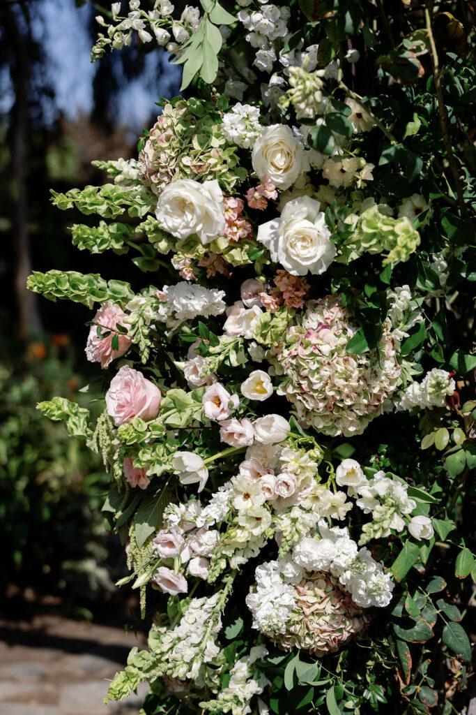 Close-up of garden-inspired florals in soft whites, blush tones, and greenery on the ceremony arbor.