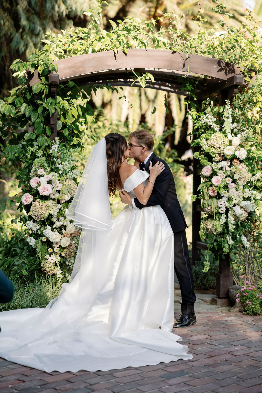 Bride and groom sharing their first kiss under a floral-covered arbor at McCormick Home Ranch.
