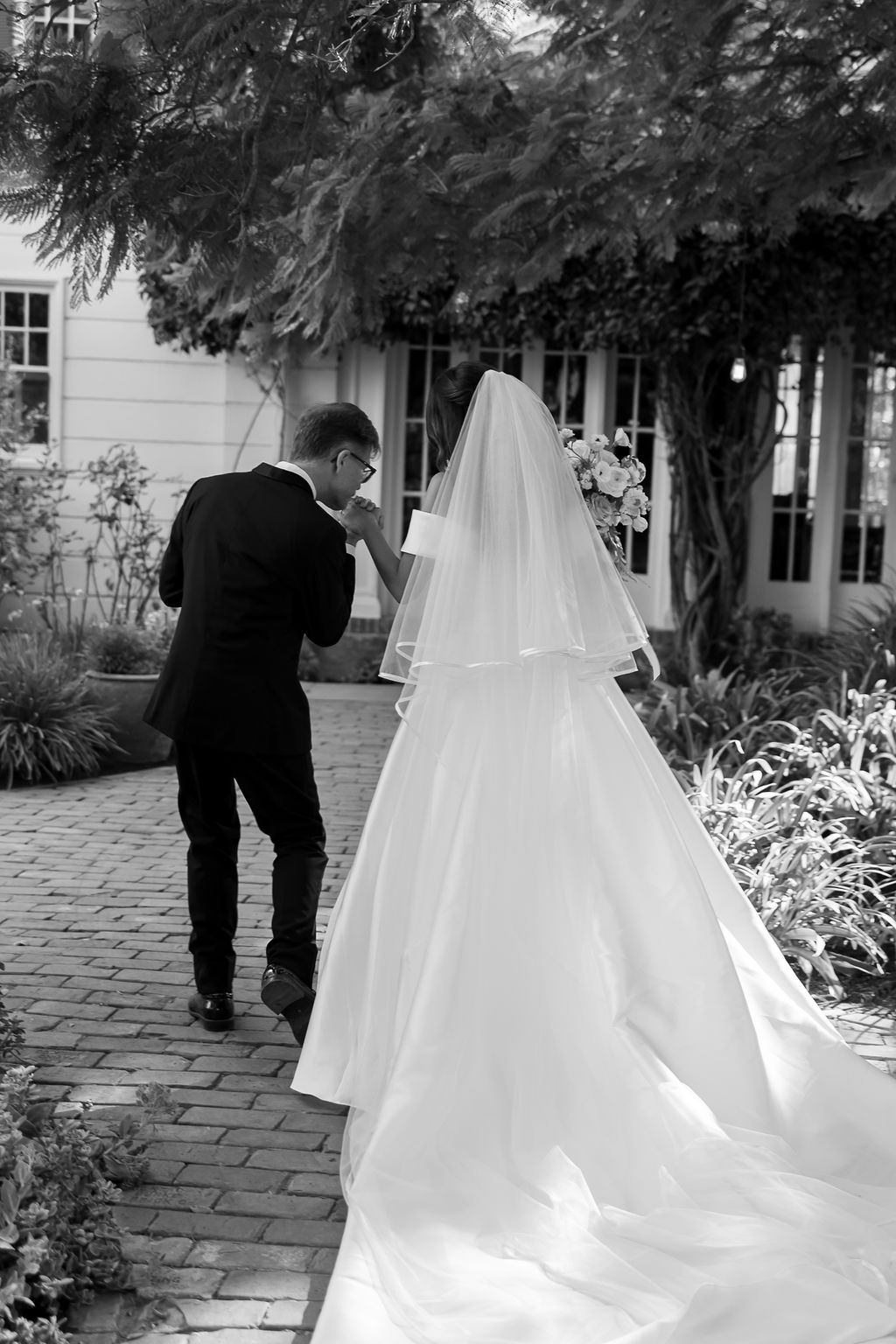 Groom lifting the bride’s hand to kiss it as they walk together after the ceremony.