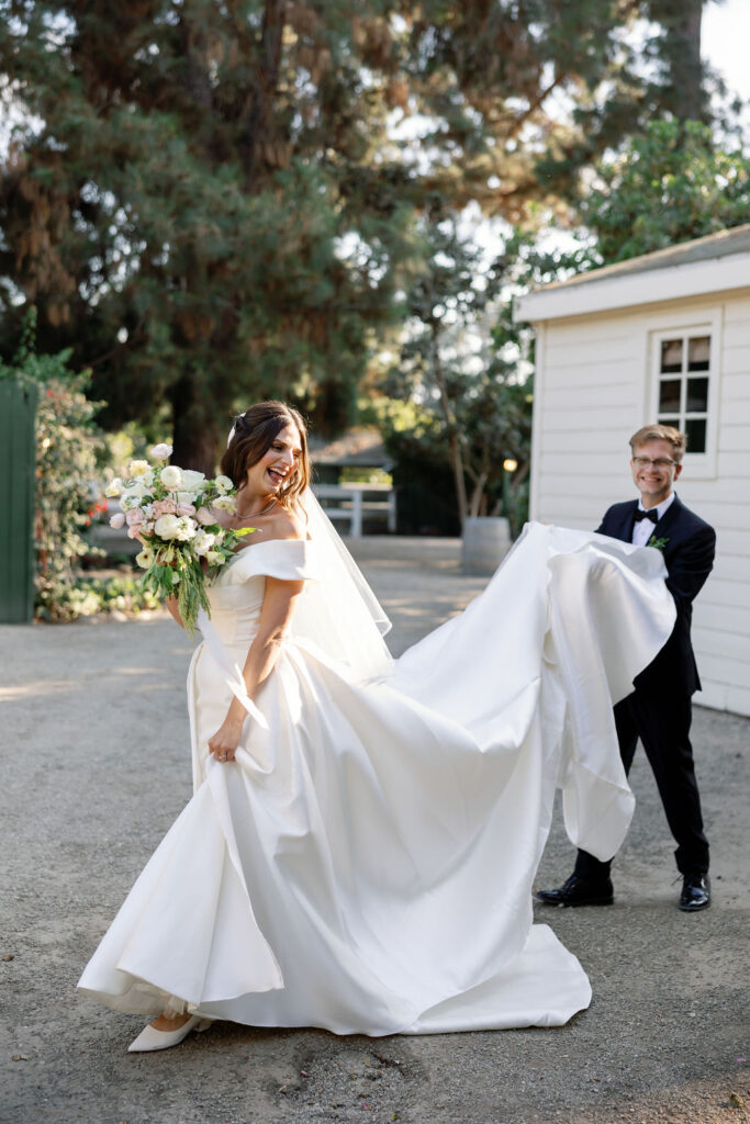 Groom holding up the bride’s dress train as she laughs and walks outside following the ceremony.
