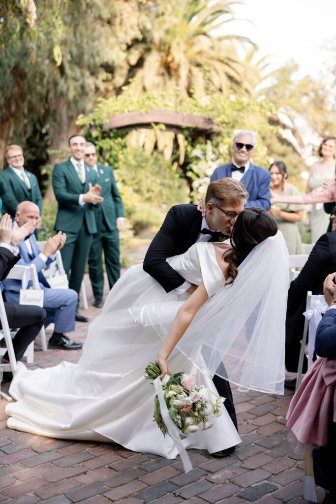 Bride and grooms end of aisle dip kiss during their outdoor McCormick Home Ranch wedding ceremony