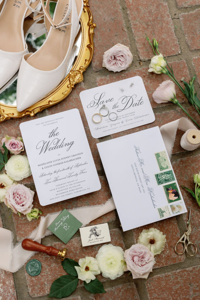 Wedding invitation suite, save-the-date card, rings, wax seal, florals, and bridal shoes arranged on brick for detail photos at McCormick Home Ranch.