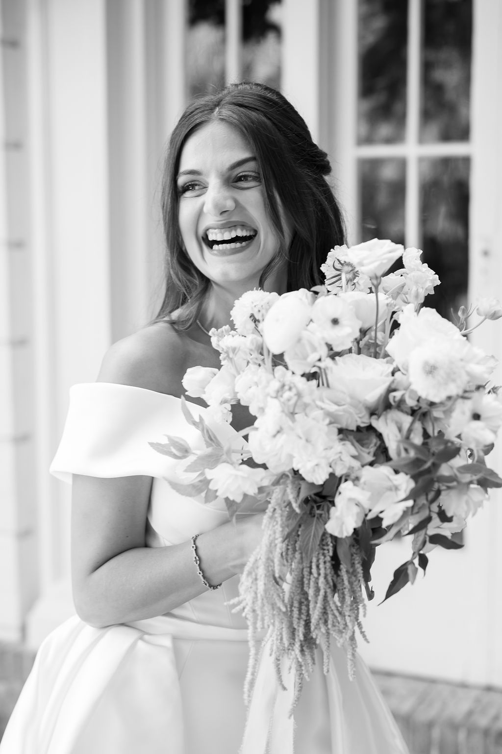 Close up black and white candid portrait of a bride laughing while holding her bouquet. 
