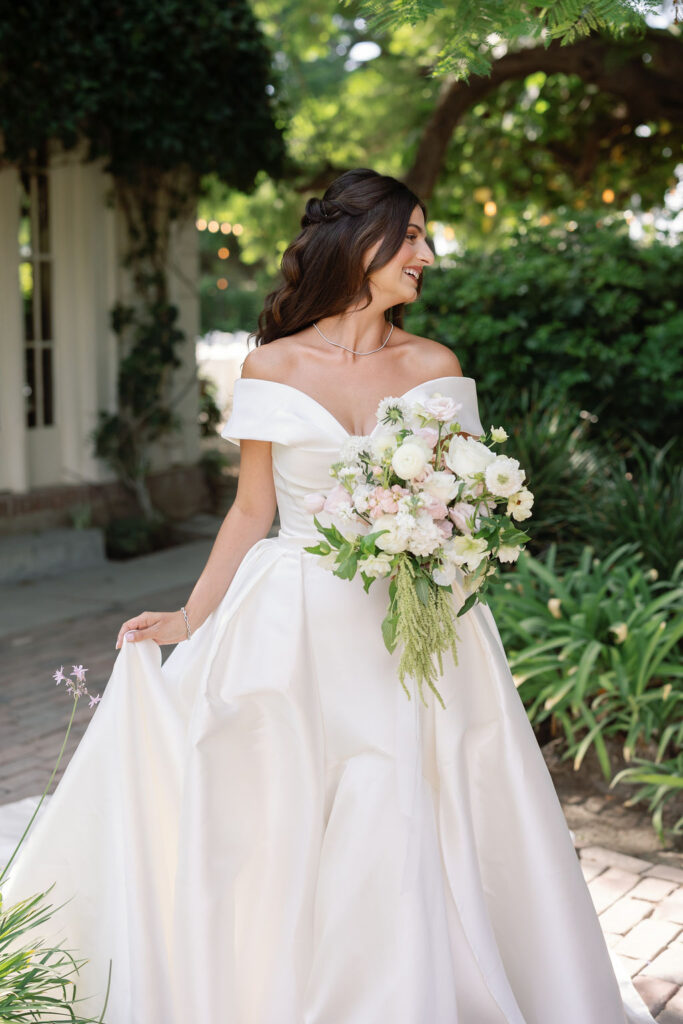 Close-up of the bride smiling and holding a bouquet of white and blush florals.