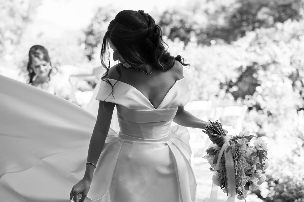 Black and white photo of a bride walking with a bridesmaid holding her train.