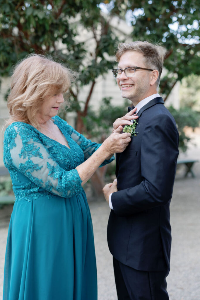 Groom smiling as his mother adjusts his boutonniere.