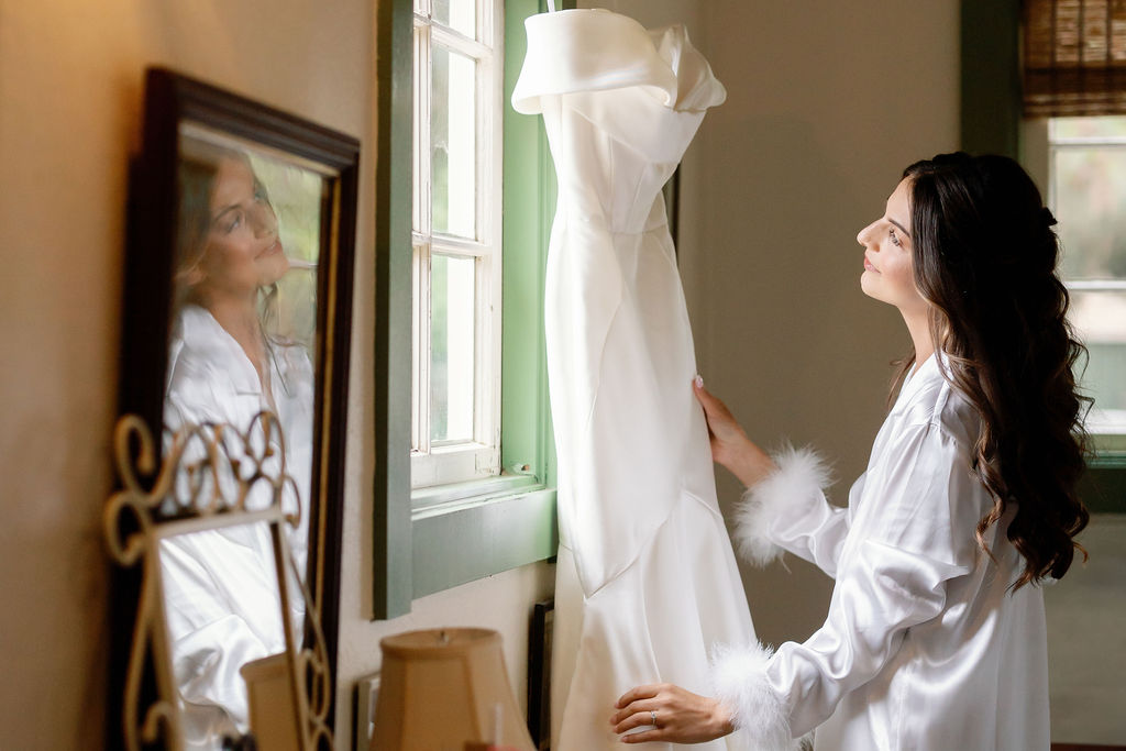 Bride smiling up at her wedding gown as she gets ready