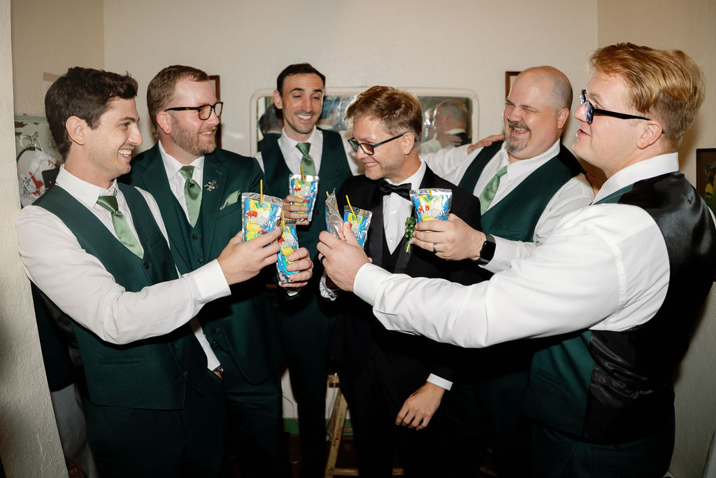 Groom and groomsmen laughing and raising Capri Suns together while getting ready.