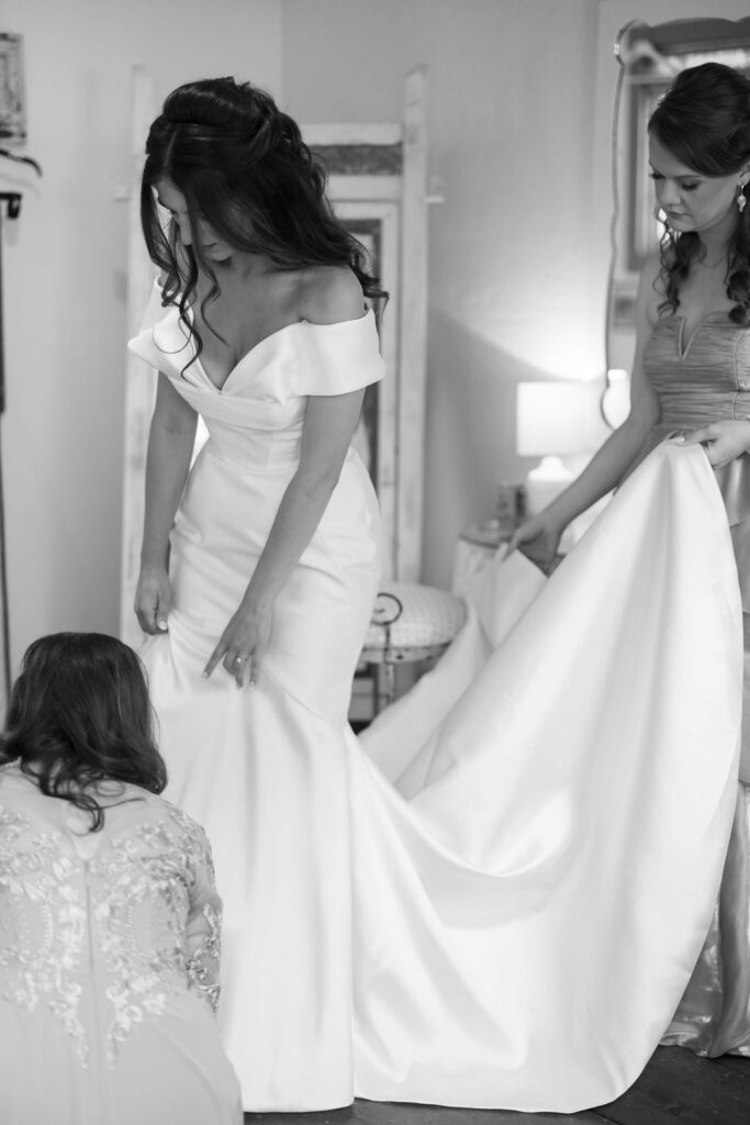 Black and white photo of the bride getting her dress adjusted.