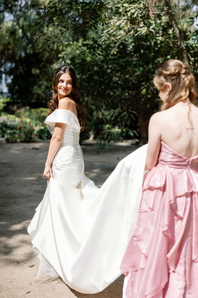 Bride looking back and smiling at her bridesmaids as they carry the train of her wedding dress