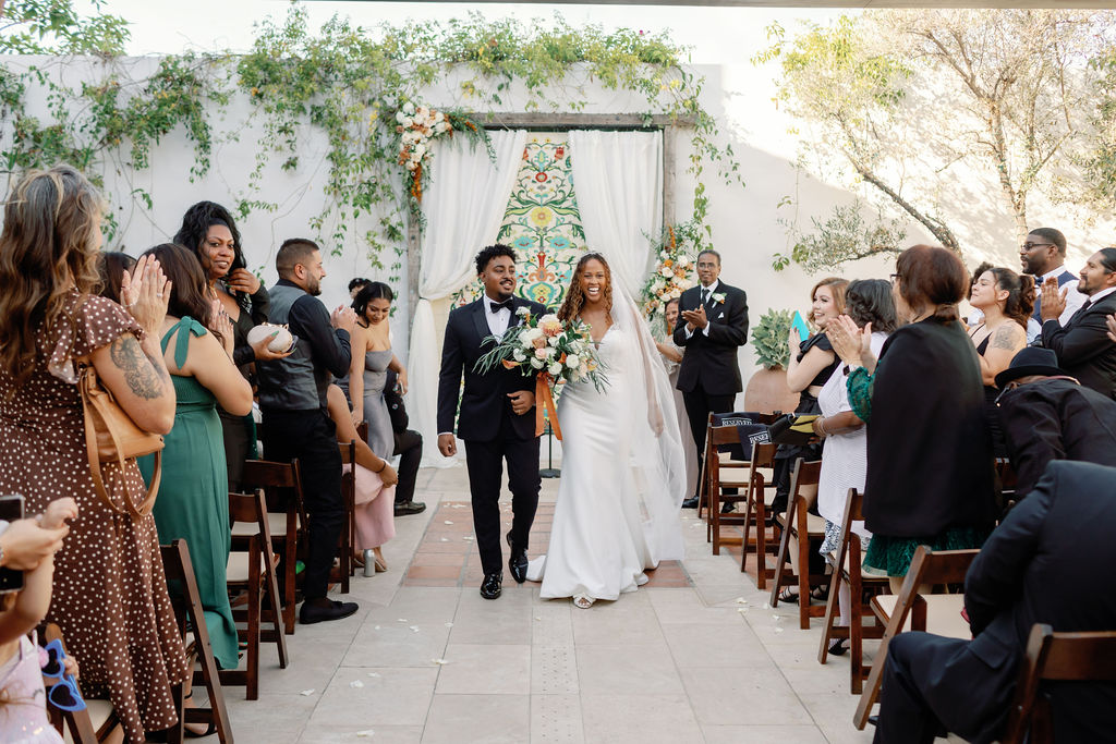 Bride and groom smiling and walking bac down the aisle after their La Ventura San Clemente wedding ceremony.