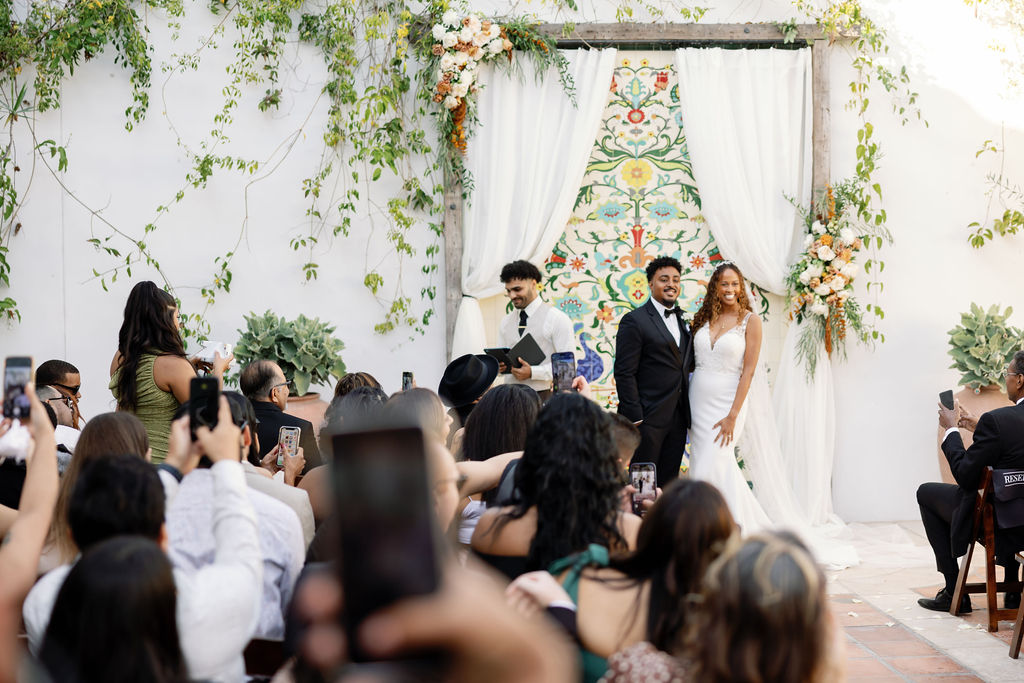 Wide shot of a bride and groom posing together for photos after their La Ventura San Clemente wedding ceremony in the courtyard.