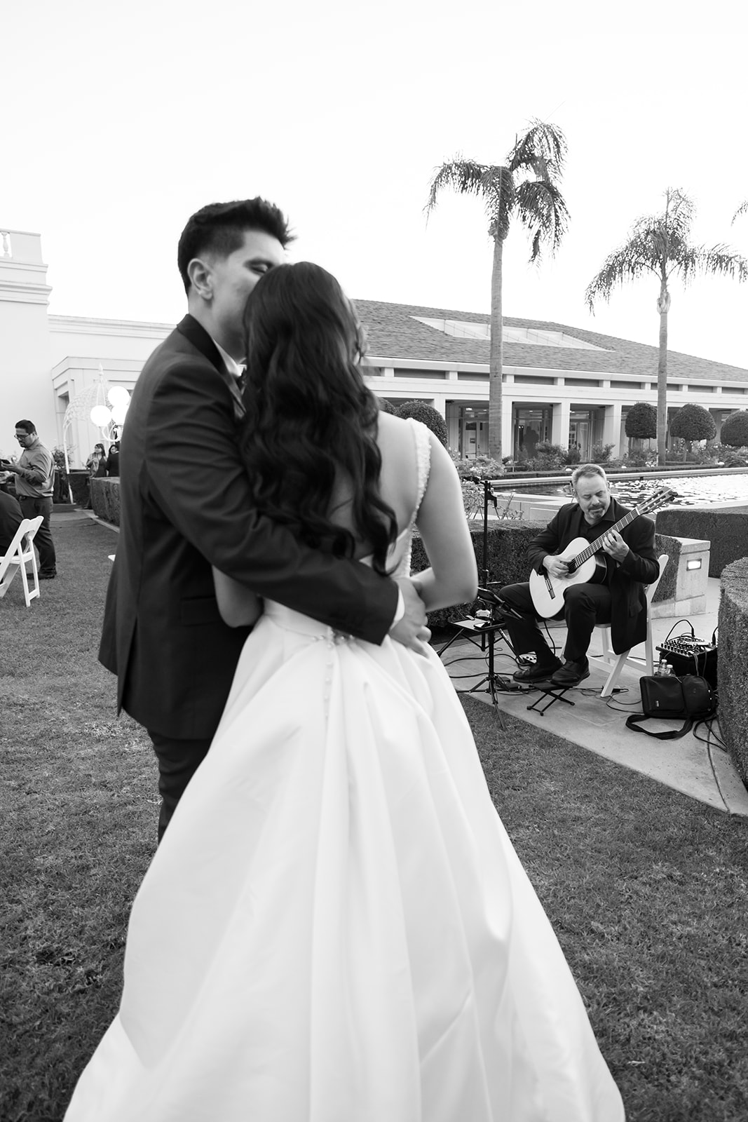 Black and white photo of a bride and groom listening to live music during their cocktail hour in the gardens.