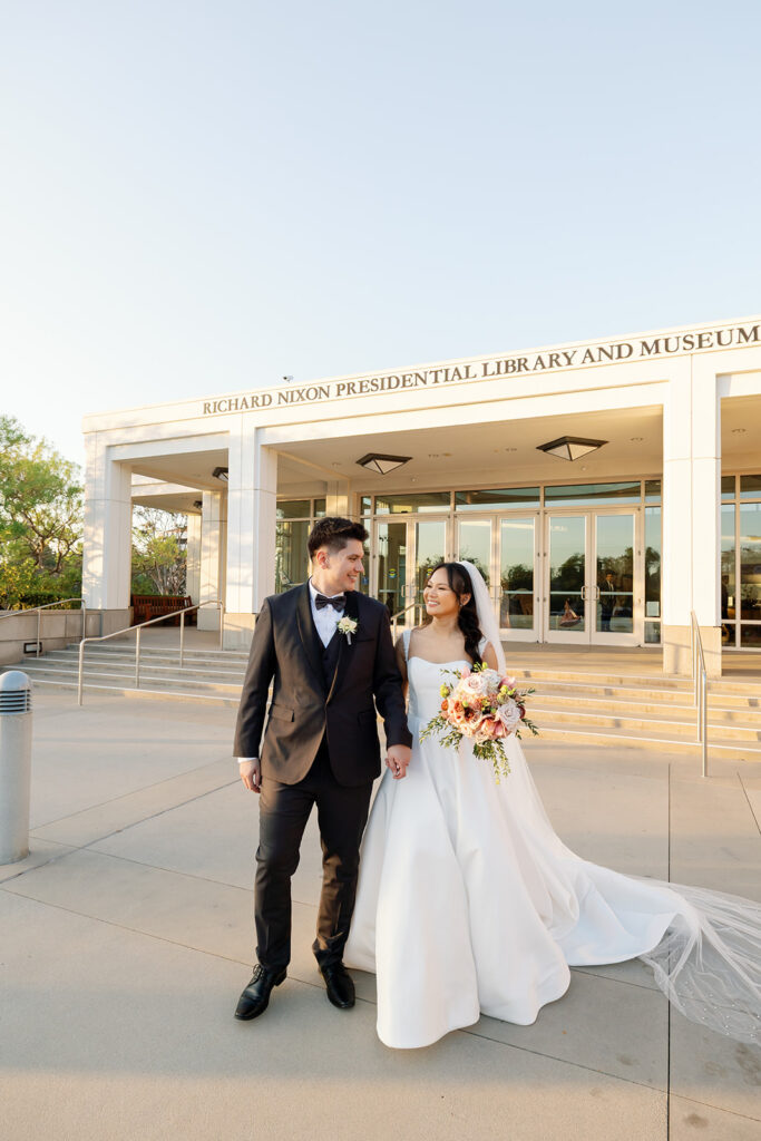 Bride and groom walking together outside the Richard Nixon Presidential Library during golden hour portraits.