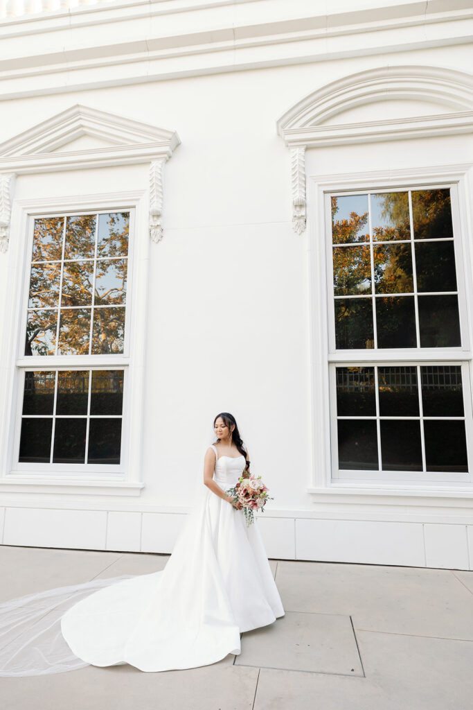 Bride posing in front of the white exterior of the Nixon Library during newlywed portraits.