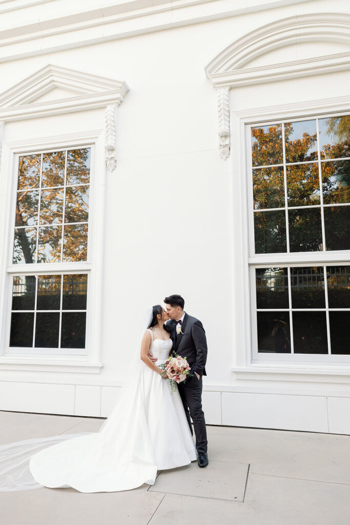 Bride and groom posing in front of the white exterior of the Nixon Library during newlywed portraits.