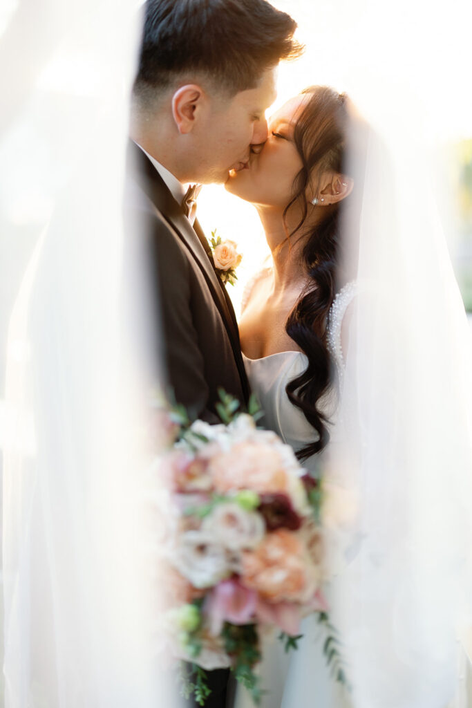 Bride and groom kissing between the bride’s veil during golden hour at Nixon Library Yorba Linda wedding.