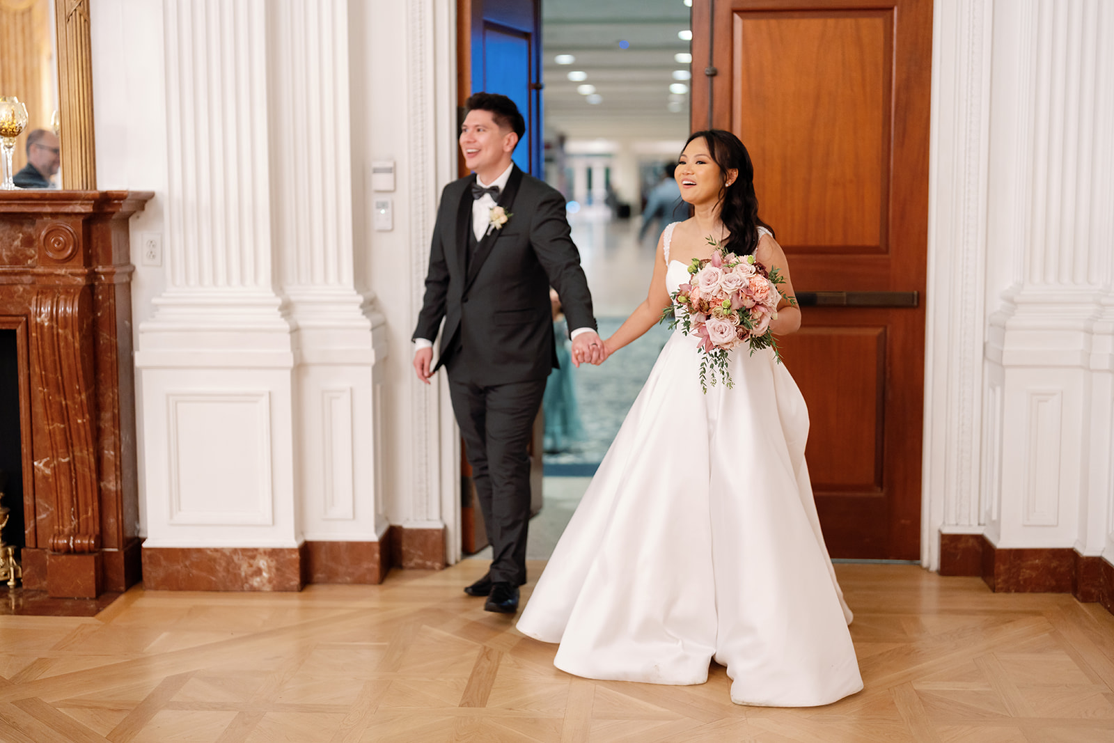 Bride and groom holding hands as they enter the East Room for their reception room reveal at a Nixon Library Yorba Linda wedding.