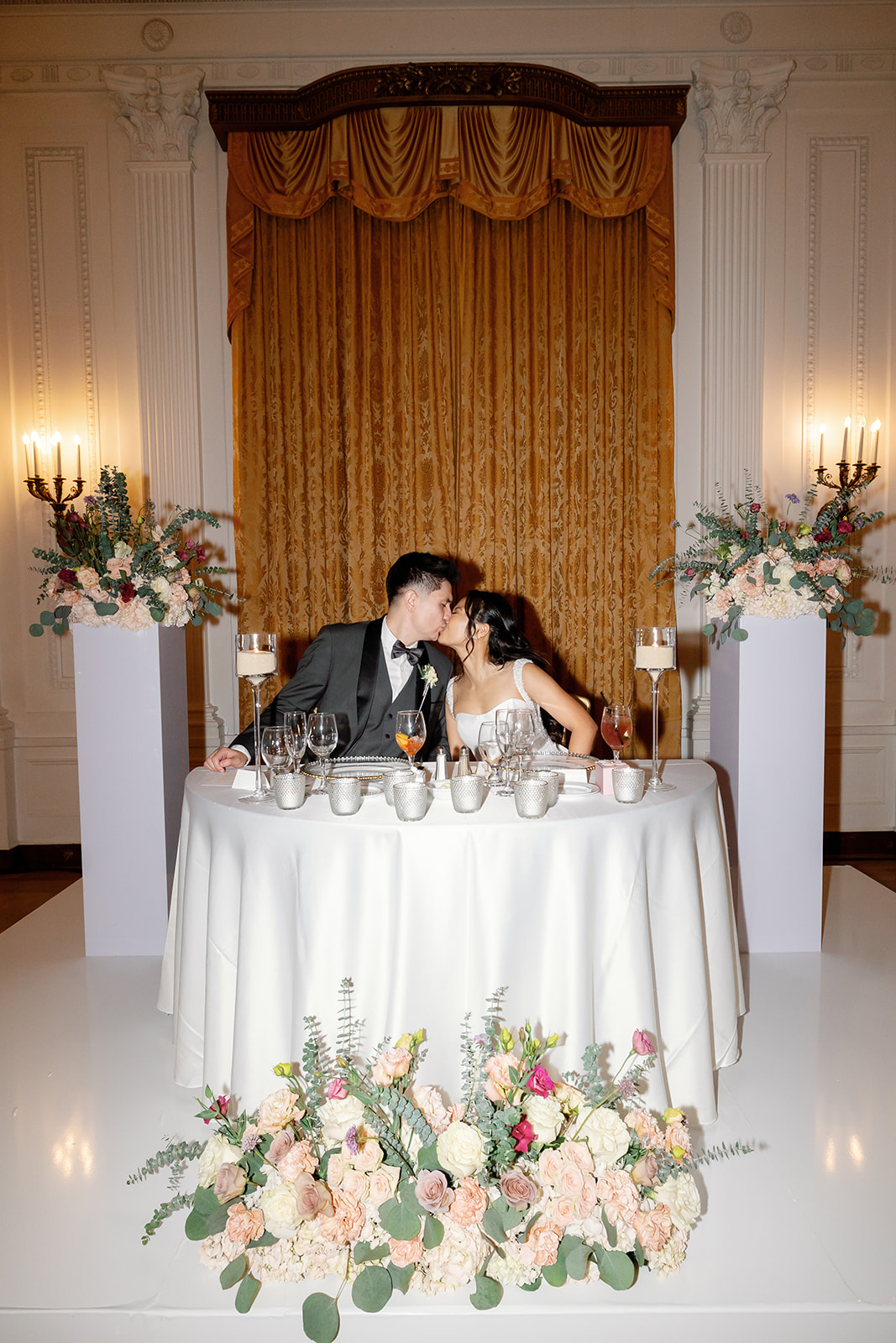 Flash wedding reception photo of a bride and groom kissing at the sweethearts table.