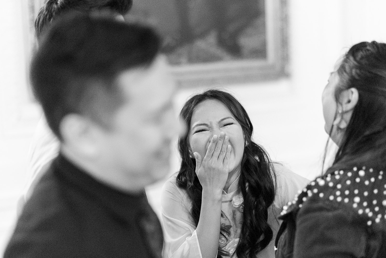 Black and white candid wedding photo of a bride laughing during speeches.