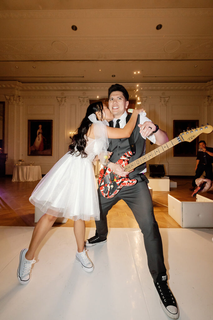 Bride kissing the groom while he plays guitar during their reception.