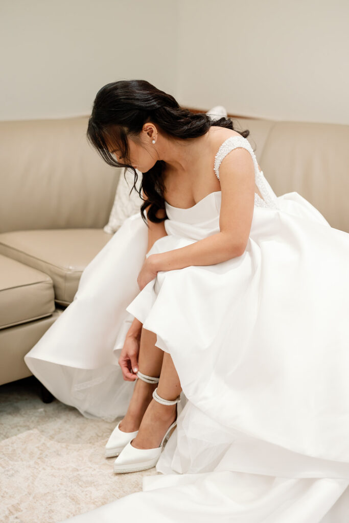 Bride sitting on a couch while putting on her wedding shoes during Nixon Library Yorba Linda wedding getting ready.