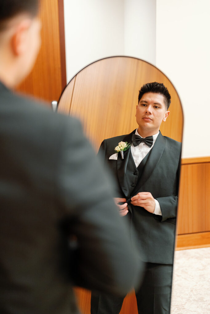 Groom adjusting his tuxedo while looking in a mirror during Nixon Library Yorba Linda wedding getting ready.