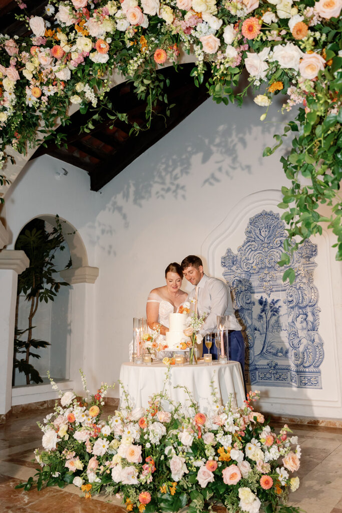 Bride and groom cutting their wedding cake beneath a floral installation at Rancho Las Lomas.