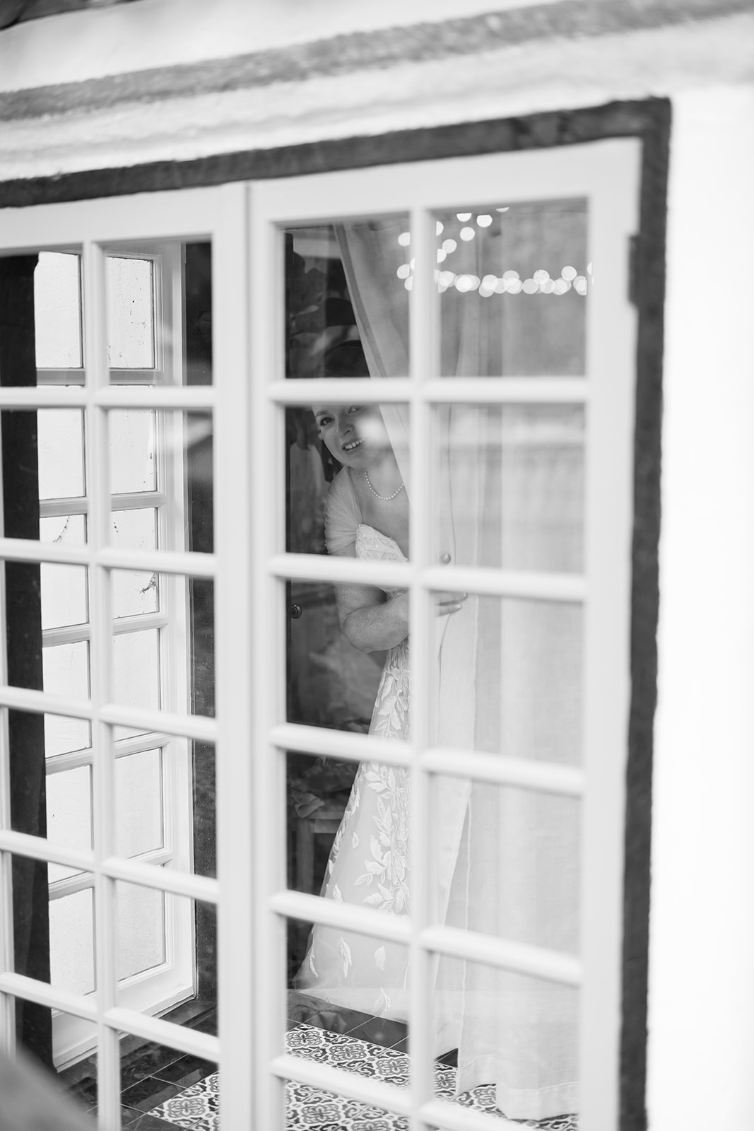 Black and white candid photo of a bride looking out a mirror at the ceremony space.