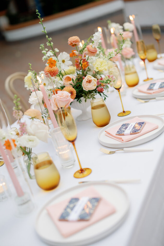 Close-up of citrus-toned floral arrangements and amber glassware on a reception table at Rancho Las Lomas wedding.