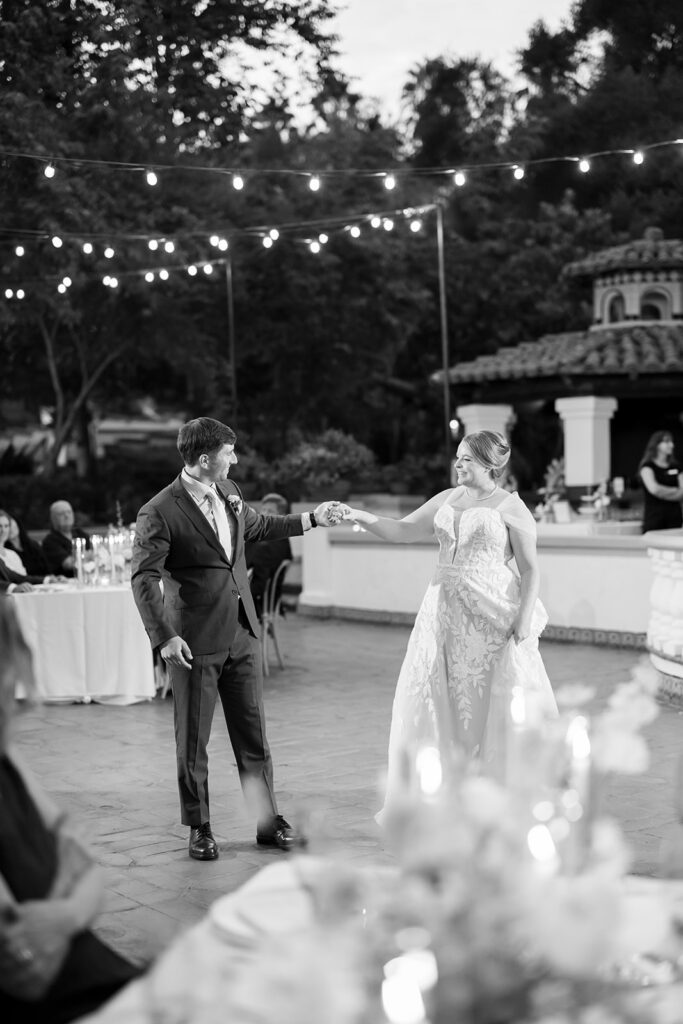 Bride and groom dancing hand in hand under café lights at El Teatro during their Rancho Las Lomas wedding.