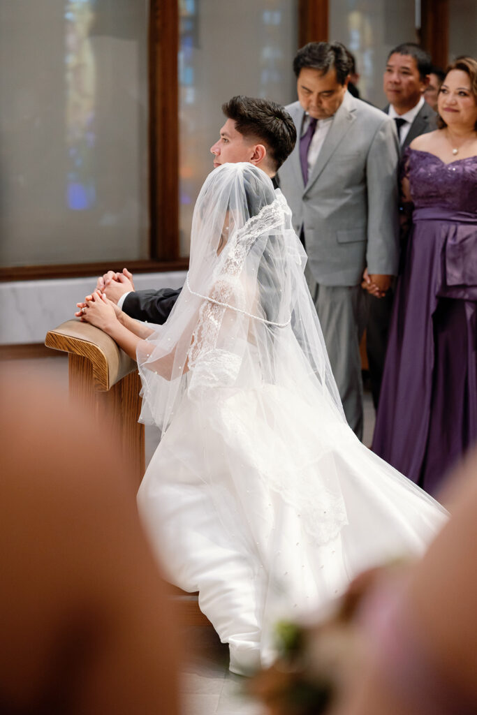 Bride kneeling in prayer beside her groom during the ceremony at St. Martin de Porres Church in Yorba Linda.