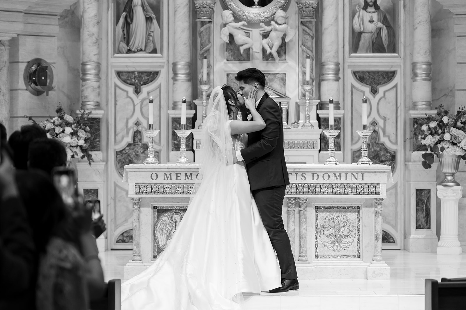 Black and white photo of the couple sharing their first kiss at the altar during their church wedding ceremony.