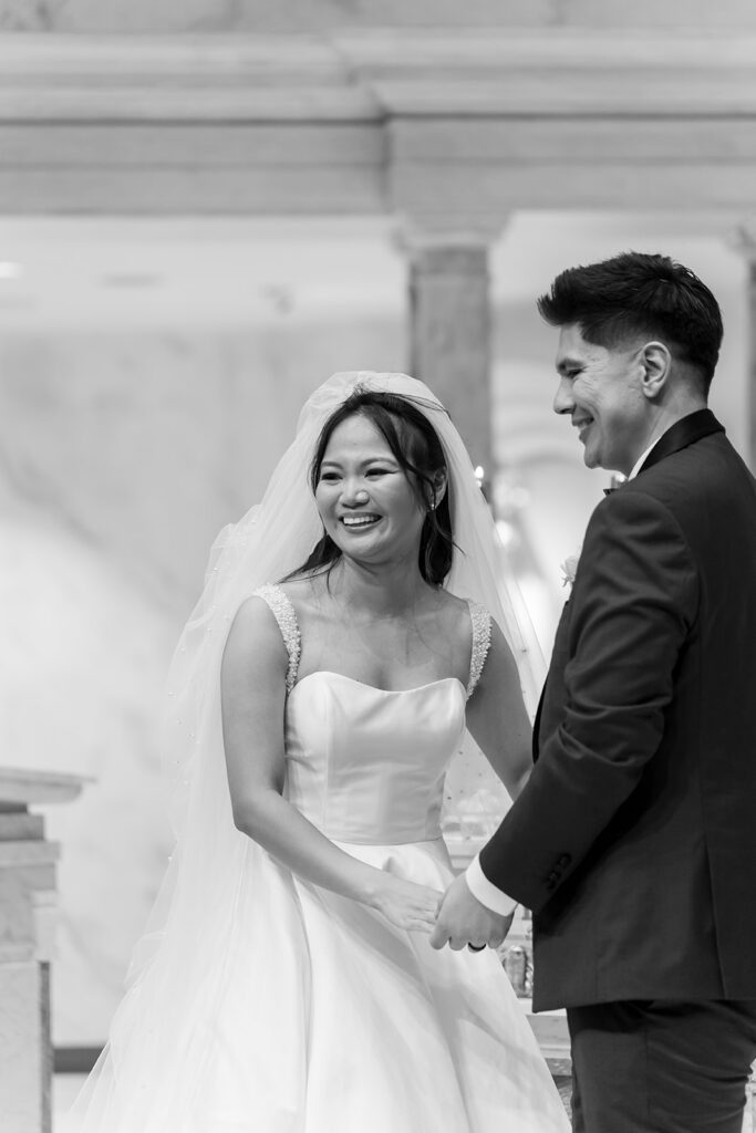 Bride and groom holding hands and smiling during their wedding ceremony at St. Martin de Porres Church.