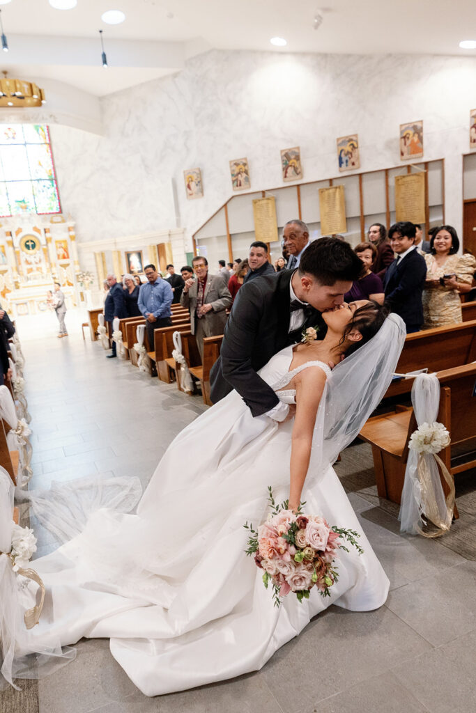 Emotional aisle dip and kiss as the couple exits the church following their wedding ceremony.