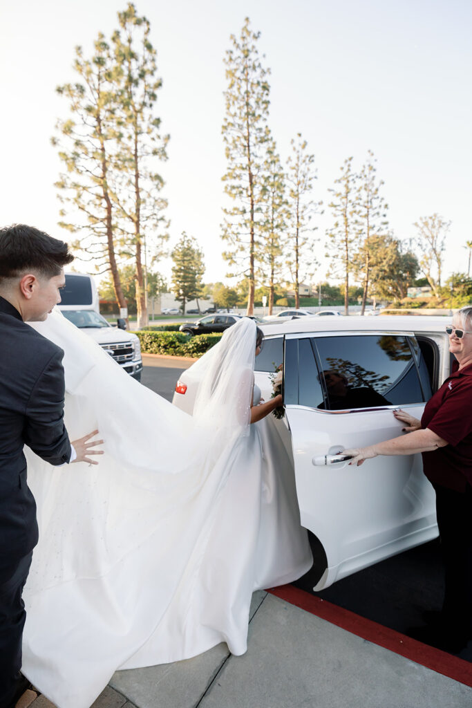 Bride being helped into the car after the ceremony, her veil flowing as she departs the church with her groom.