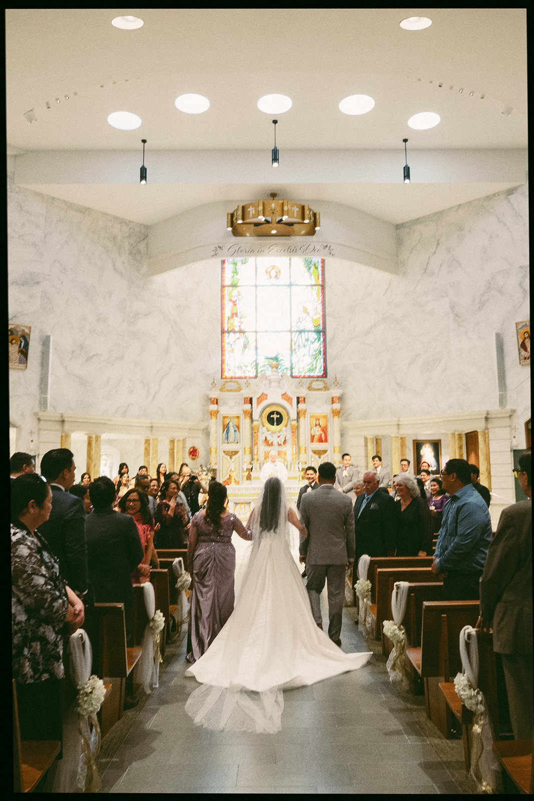 Film photo of a bride walking to the altar with her parents for a St. Martin de Porres Church wedding ceremony in Yorba Linda.