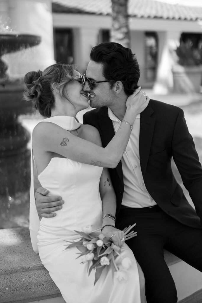 Black and white portrait of a bride and groom kissing with sunglasses on.