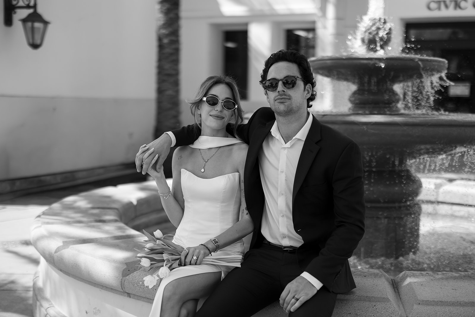 Bride and groom sitting by fountain outside Laguna Hills Civic Center during elopement portraits.